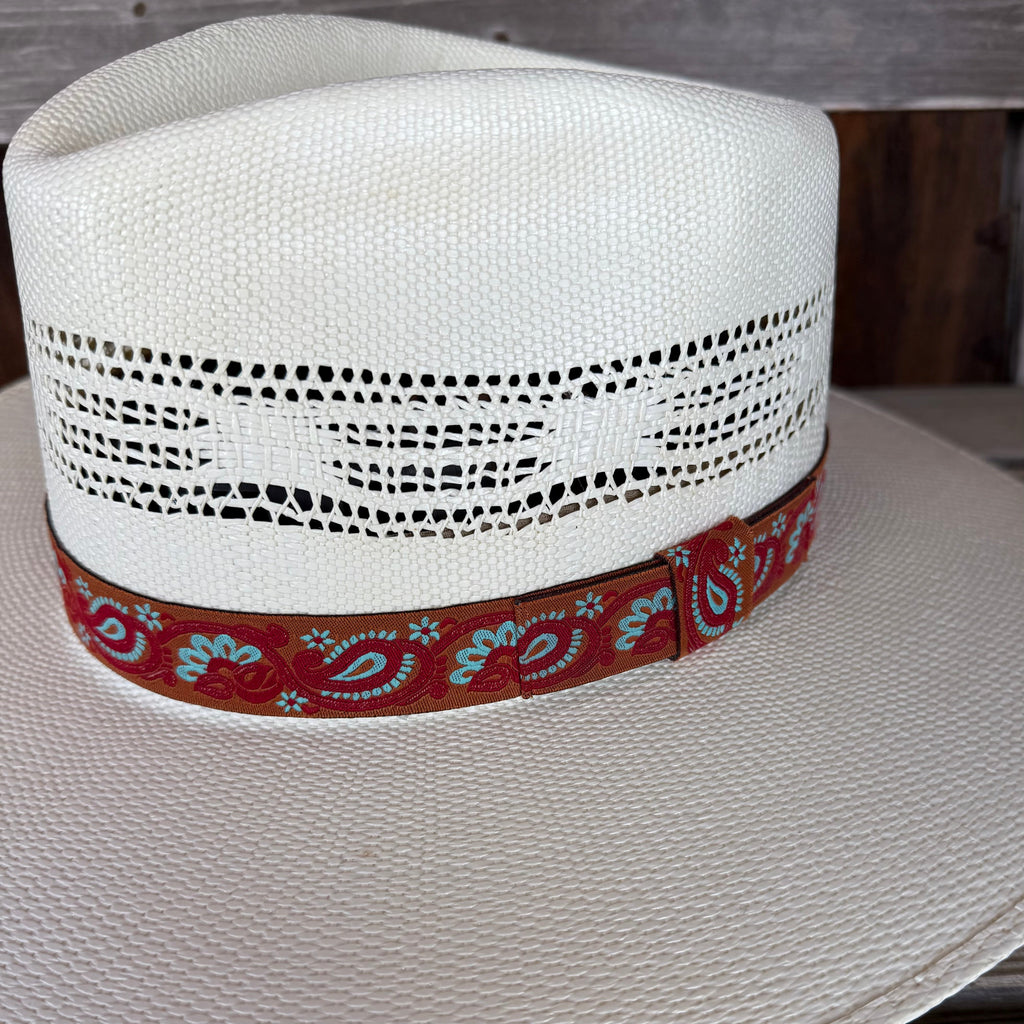 White straw hat with a red band featuring blue patterns on a wooden surface.
