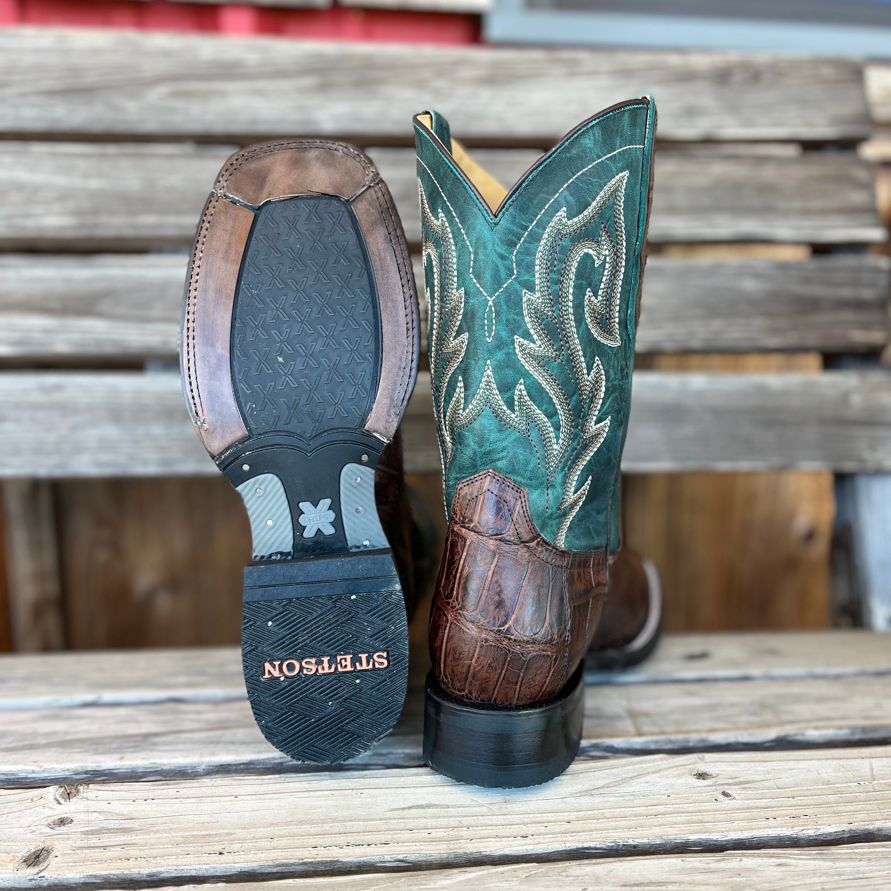 Pair of turquoise cowboy boots with detailed embroidery on a wooden surface.